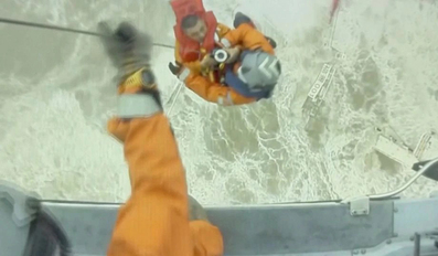 Rescuers lift a crew member of a sinking vessel into a helicopter